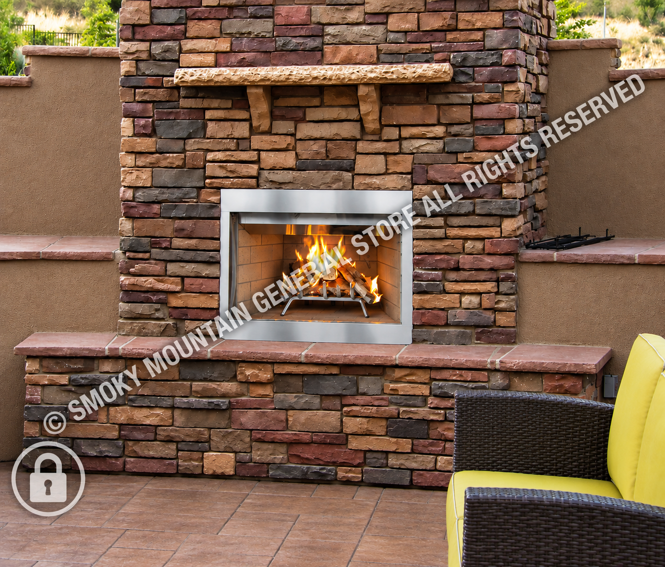 A built-in outdoor fireplace with a rectangular stainless steel firebox and visible flames, set into a stacked stone wall with a stone mantel and brick hearth.